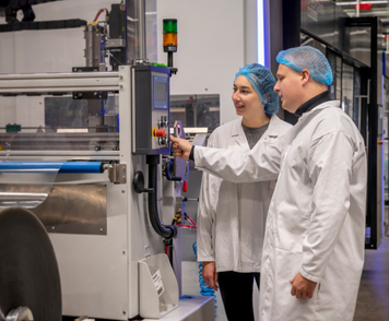 Operators in white coats operate a packaging machine together in a clean production environment