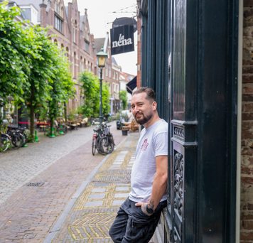 Kandidaat leunt glimlachend in deuropening van stadsgebouw.